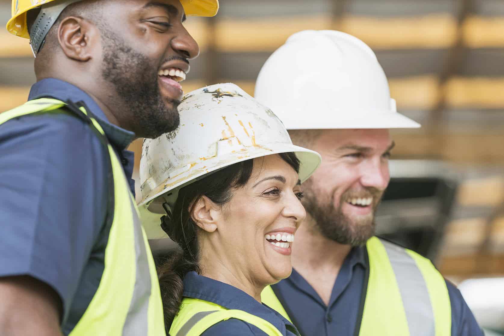 two men and a woman wearing construction hats and laughing