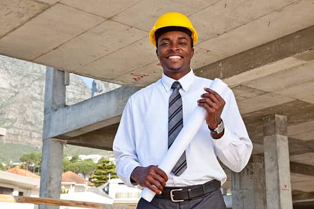 African man in a suit and construction hat holding architecture plans on site