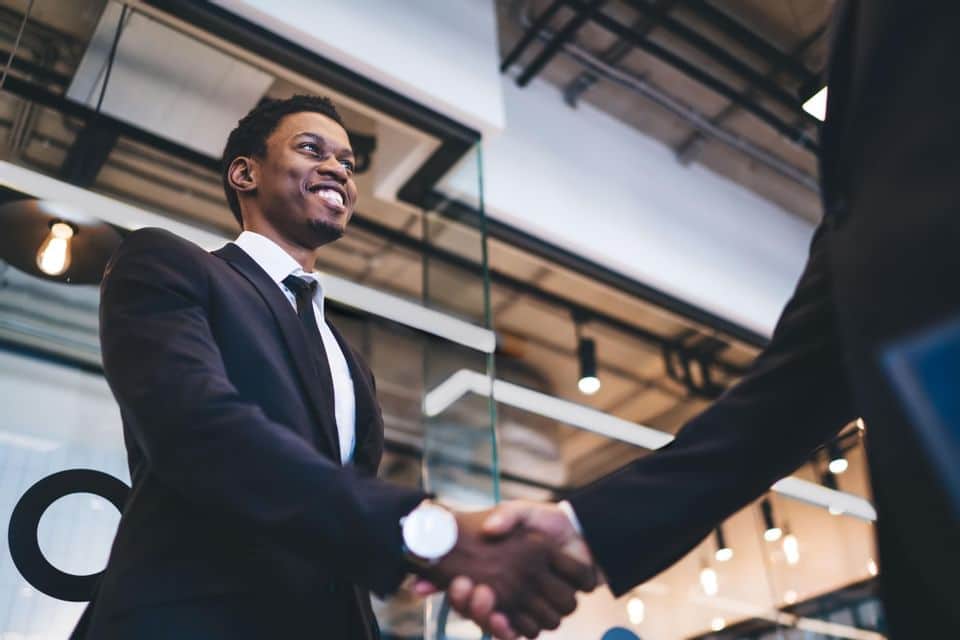 smiling black man in a suit and tie shaking the hand of other man